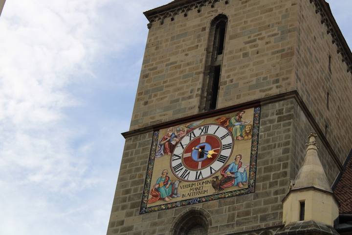Colorful medieval clock face on a tall stone church tower against a blue sky.