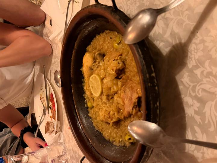 Traditional Moroccan chicken tagine served in an earthenware dish on a restaurant table with diners seated around.