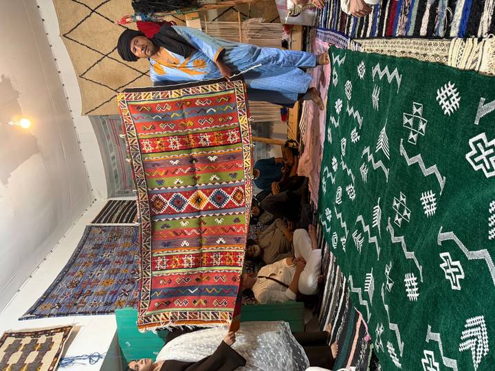 Local presenter displaying a colorful hand-woven rug to a seated group inside a carpet cooperative.