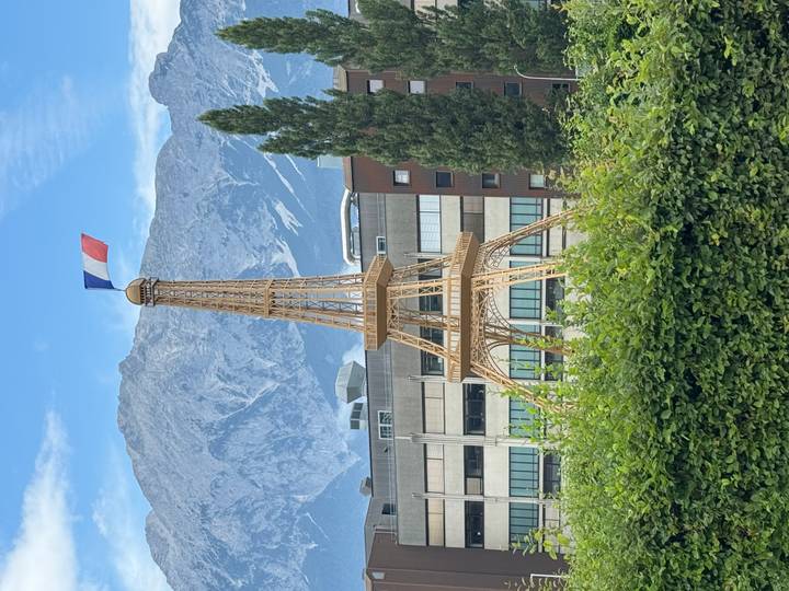 Small wooden replica of the Eiffel Tower with a French flag set in front of alpine mountains and offices