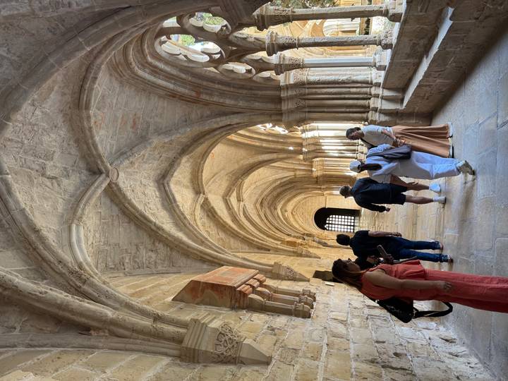 Visitors exploring a stone Gothic cloister with vaulted ceilings and warm lighting