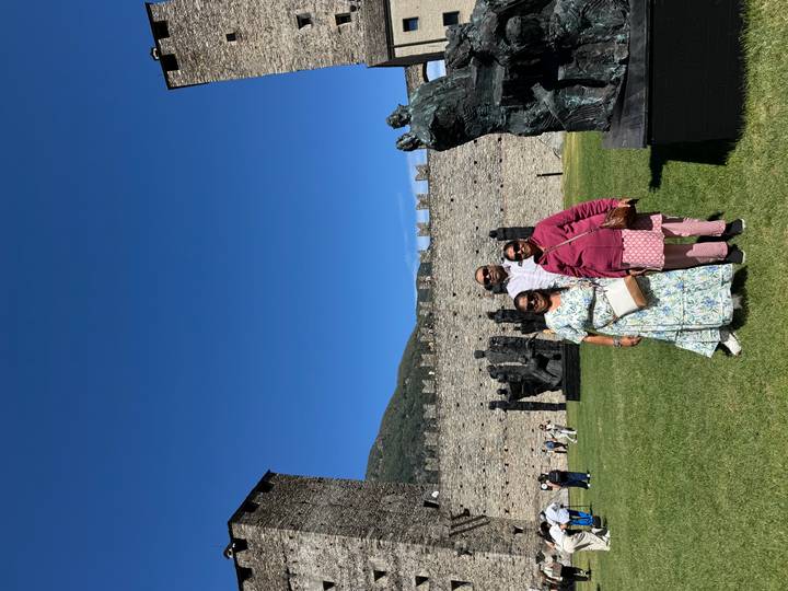 Family posing on lawn beside medieval stone walls and sculptures under blue sky