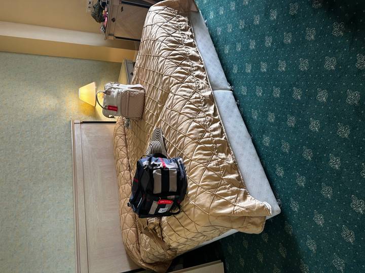 Hotel bedroom with personal luggage and hat placed on a quilted bedspread.