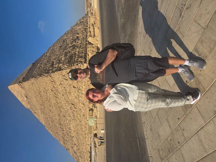 Tourists pose in front of the Great Pyramid of Giza under a clear blue sky