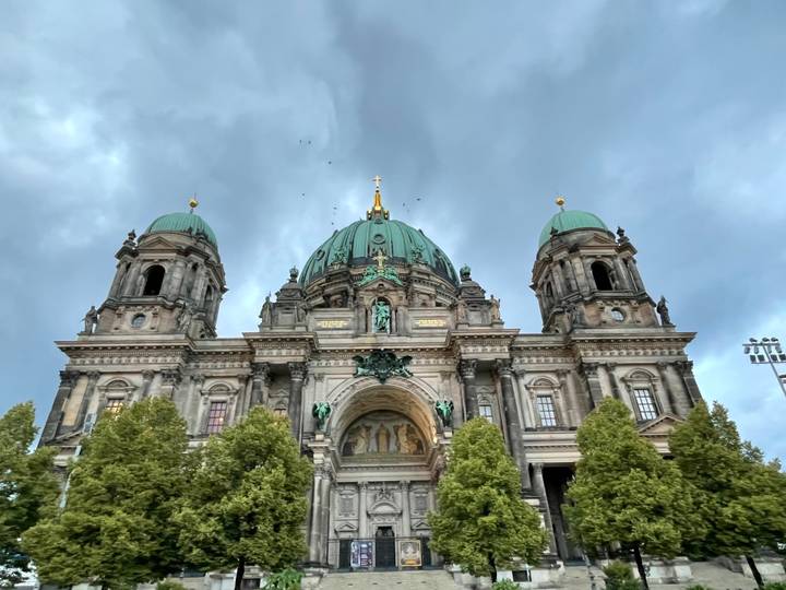Front view of Berlin Cathedral with dramatic clouds and green copper domes.