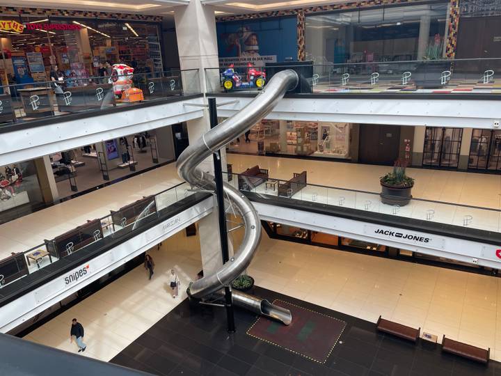 Interior atrium of a shopping mall featuring a long spiral slide between floors.