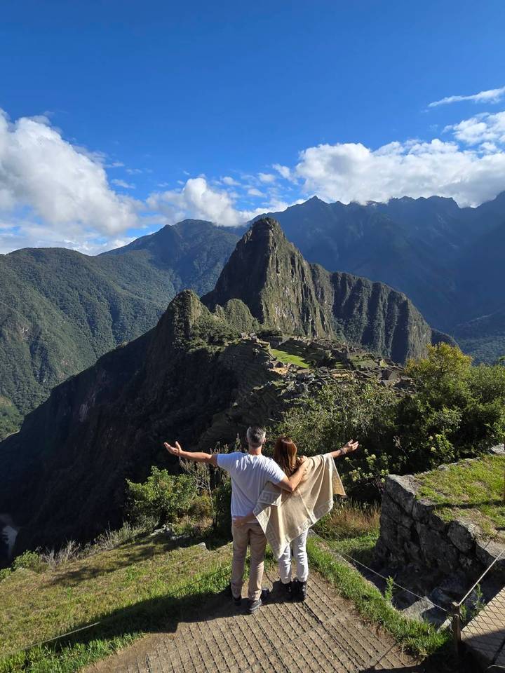 Couple with outstretched arms admiring the iconic terraces and peak of Machu Picchu from a high viewpoint