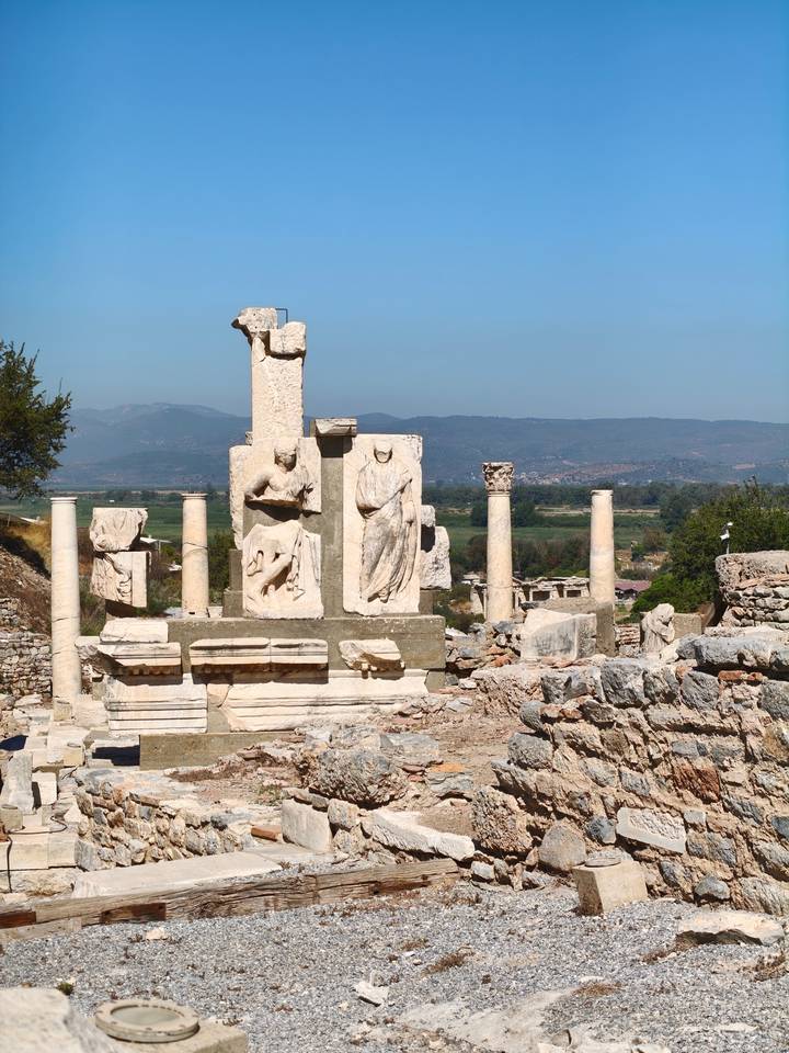 Ancient marble columns and reliefs of Ephesus rise against a clear blue Anatolian sky.