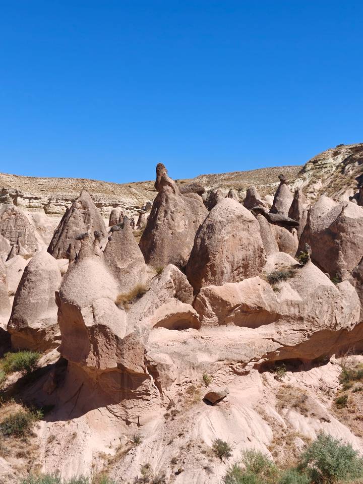 Pink-tinted rock pinnacles and fairy chimneys rise sharply against a clear Cappadocia sky.
