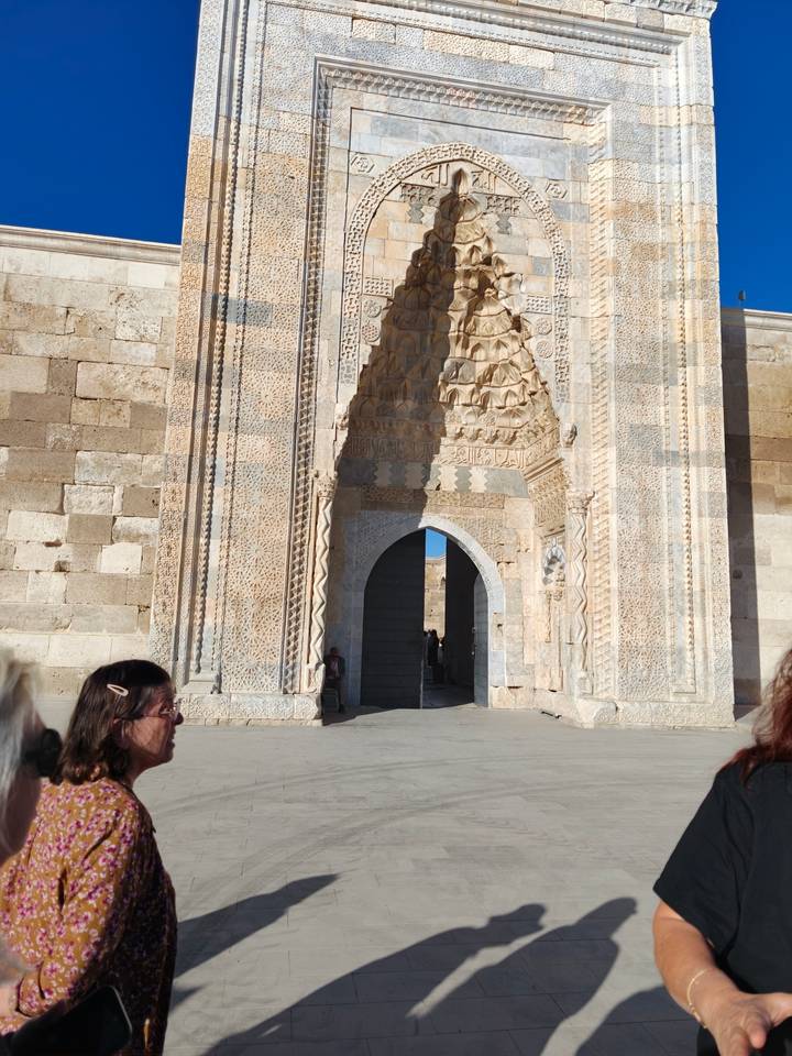 Intricately carved Seljuk caravanserai gateway with tourists admiring the stone details.