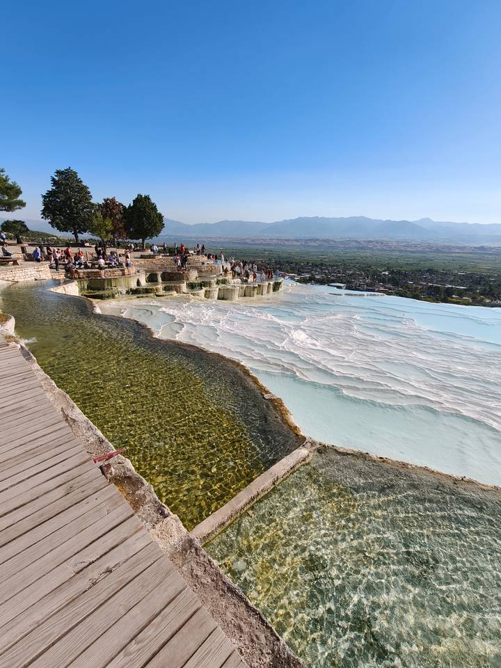 White travertine terraces overflow with turquoise water overlooking a valley filled with visitors.