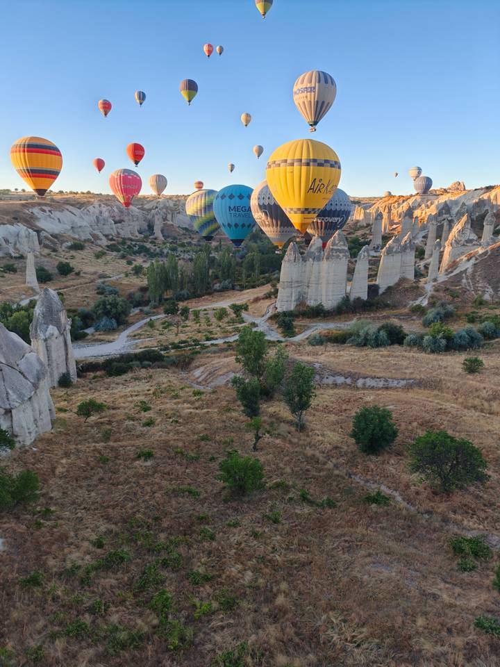 Colorful hot-air balloons drift above dramatic fairy chimneys and valley at early morning light.