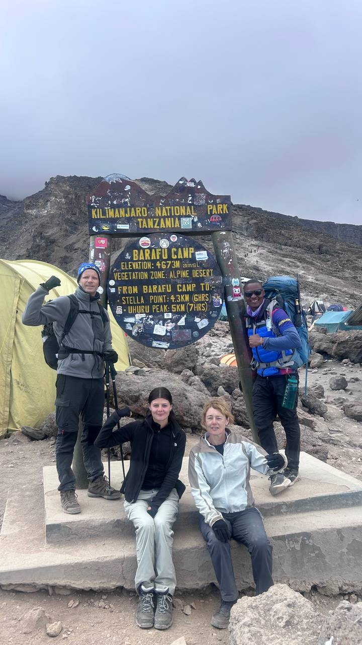 Climbing group poses beside the Barafu Camp elevation sign on Mount Kilimanjaro.