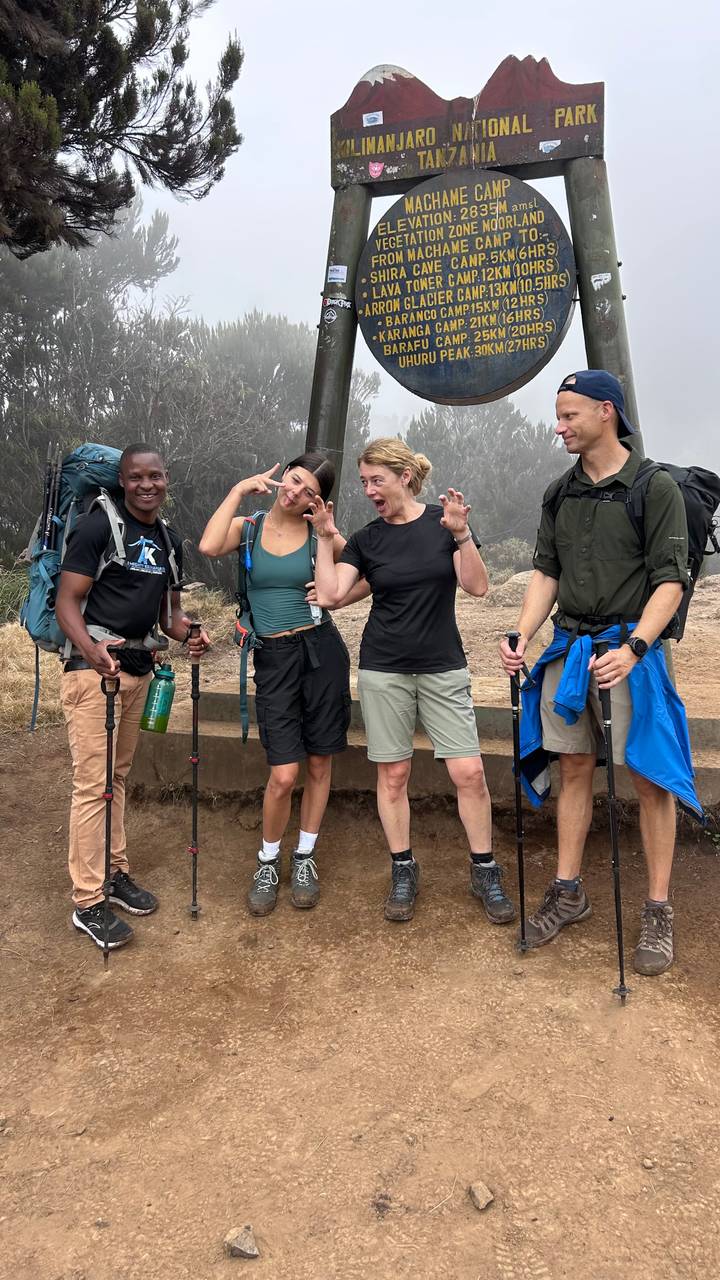 Trekking friends make playful faces with trekking poles amidst misty Kilimanjaro forest.