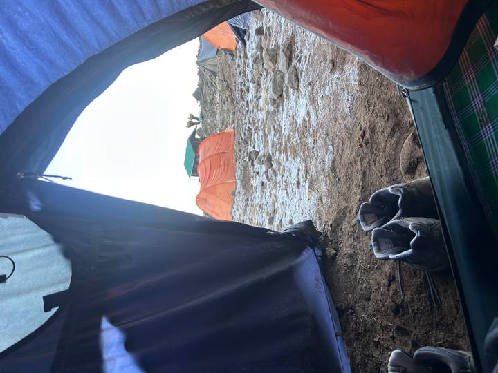 View out of a tent onto a rocky alpine campsite with orange tents and hiking boots in the foreground