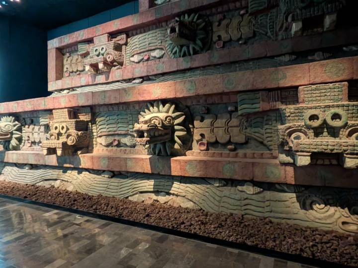 Stone serpent and mask carvings from the Temple of the Feathered Serpent displayed in museum lighting