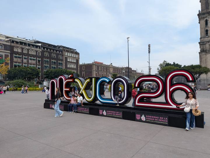 Tourists posing beside the colorful 'MÉXICO 26' sign in the main city square