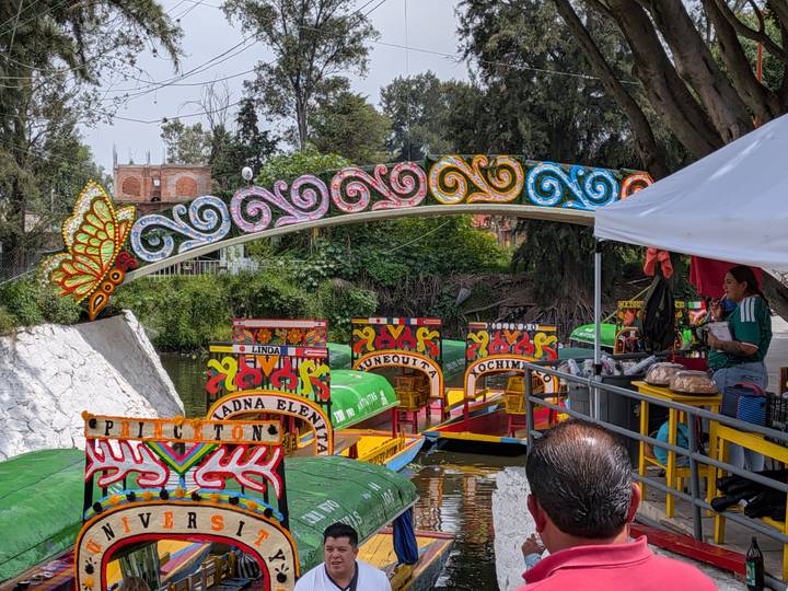 Colorful trajinera boats moored beneath a decorated bridge at Xochimilco canals