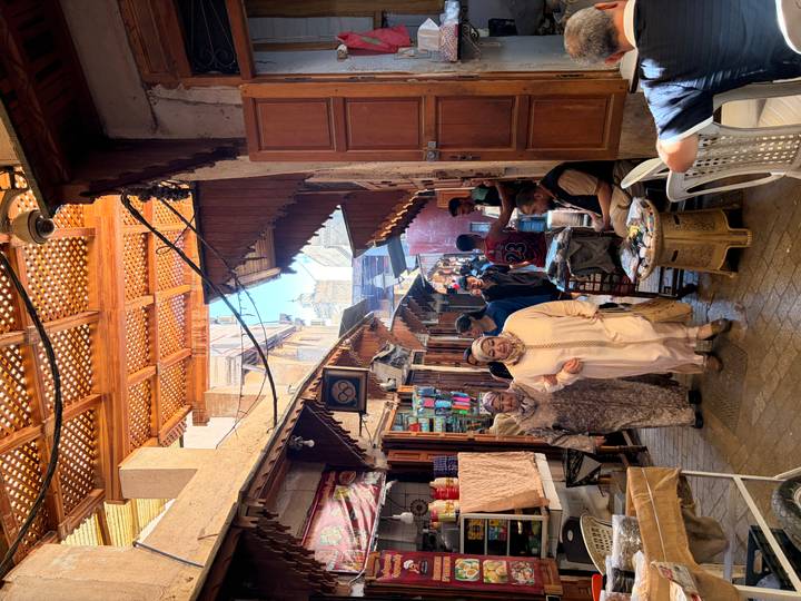 Bustling covered alley in the Fes medina with locals in traditional dress, colorful goods and carved wooden ceilings.