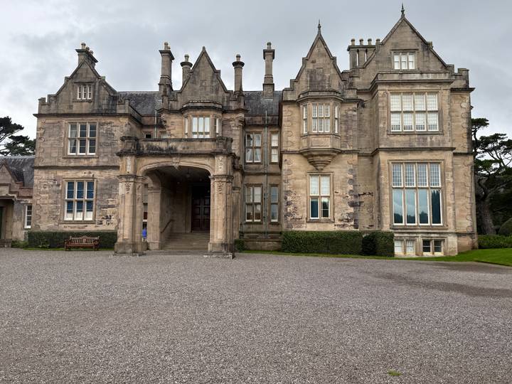 Grand Victorian manor house with stone façade, arched portico entrance and manicured hedges.