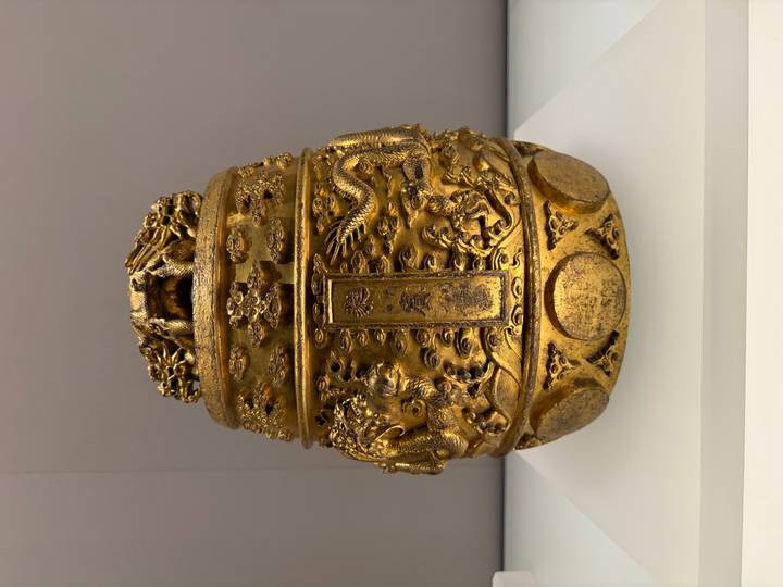 Close-up of an ornate golden Chinese ceremonial vessel with dragon motifs displayed in a museum case