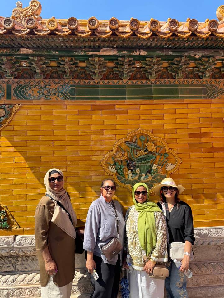 Four women stand against a vivid yellow-glazed dragon wall inside the Forbidden City.