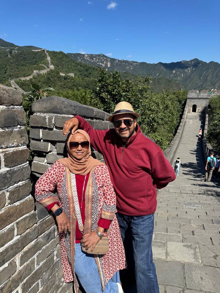 Couple poses beside the grey brick battlements of the Great Wall descending into a valley.