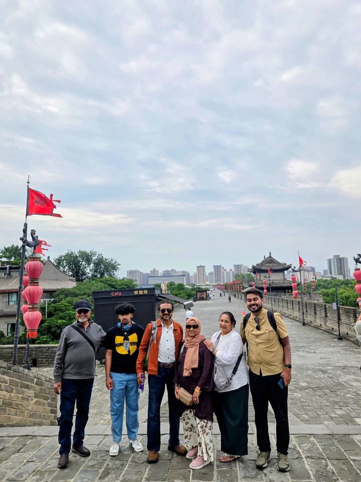 Group of travellers stands on Xi’an city wall walkway lined with red lanterns and flags.