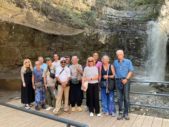 Large tour group smiling in front of a rocky waterfall inside a forested urban canyon.
