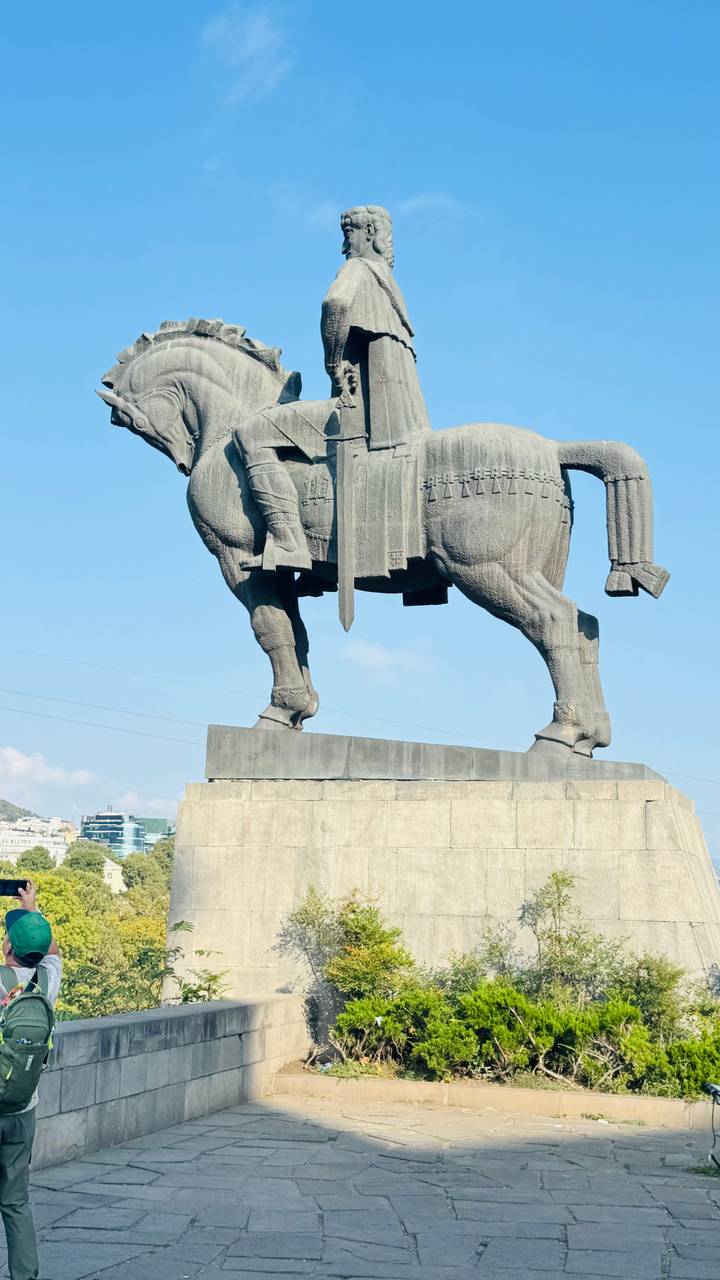 Stone equestrian statue of a medieval king against a clear blue sky.
