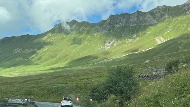 Steep alpine slopes lit by shafts of sun with a winding mountain highway below.