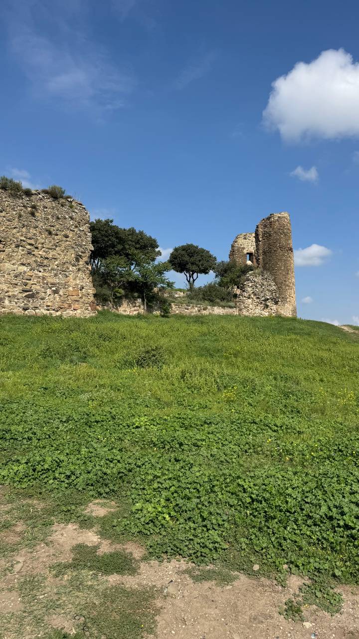 Ruins of an old stone tower and walls on a grassy hilltop under blue sky.