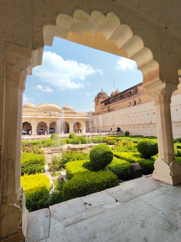Lush garden courtyard with fountains framed by palace arches under a bright sky.