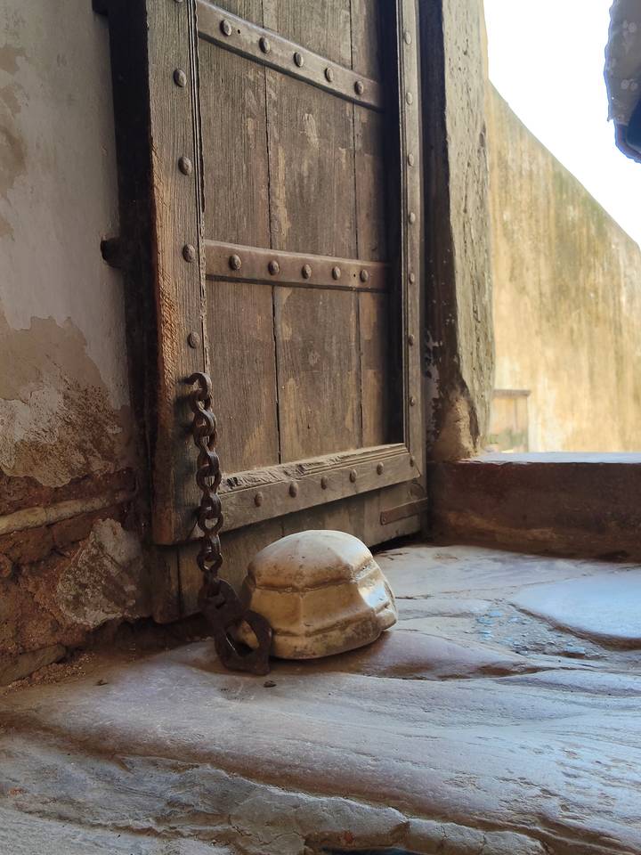 Close-up of an old wooden door with iron studs, chain and stone threshold in soft light.