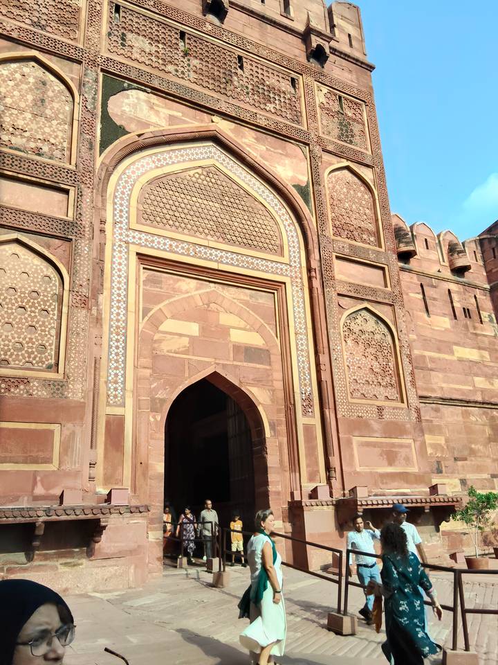 Tall ornate gateway of red sandstone with intricate inlay work in Agra Fort under blue skies.