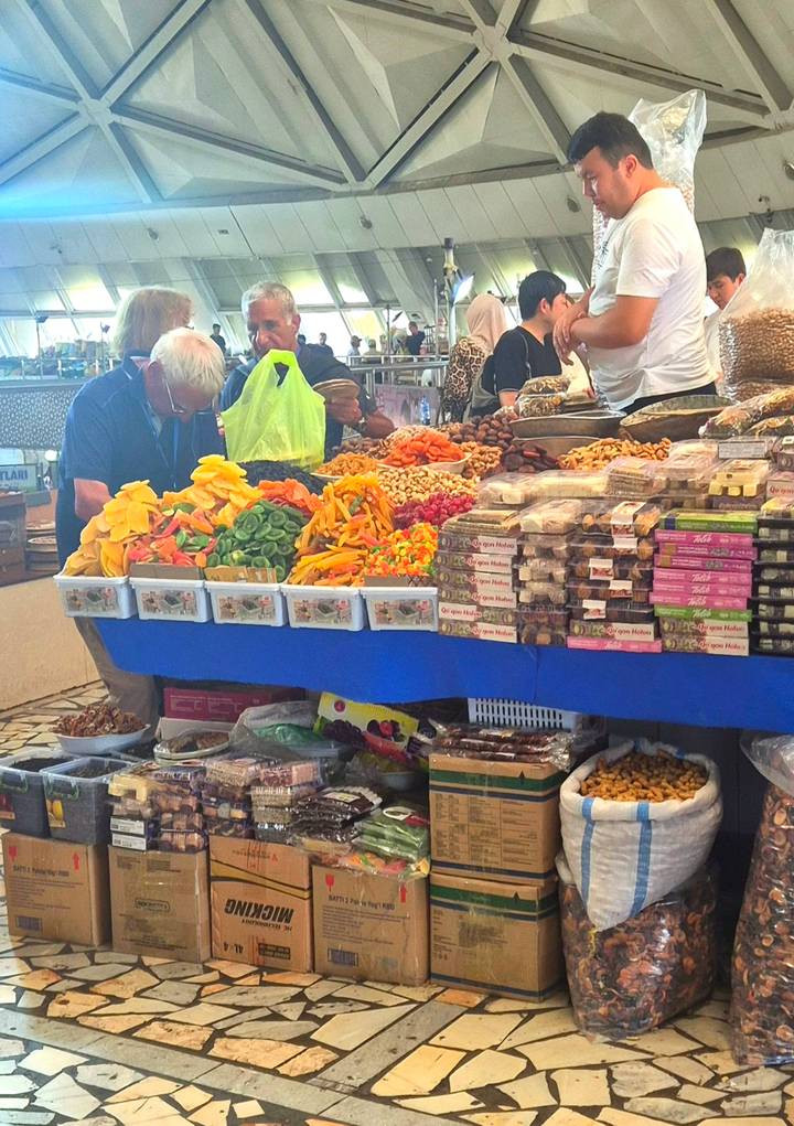 Market vendor selling dried fruits, nuts and sweets displayed in colorful heaps on a blue counter.