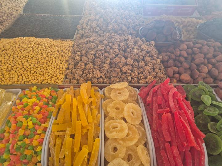 Assortment of dried fruits, nuts and candied pieces arranged in separate trays at a market.