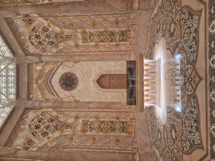 Opulent interior chamber with intricate golden mosaics, marble floor and central sarcophagus.