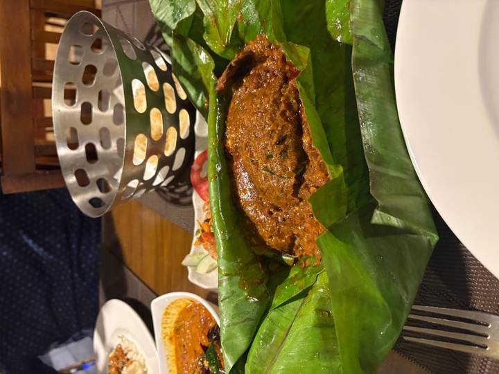 Indian dish wrapped and cooked in a banana leaf served on a restaurant table.