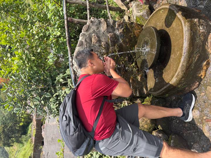 Traveler drinking cool water from a natural stone fountain along a forest trail.
