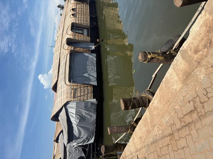 Row of covered houseboats moored on calm backwater canal under a bright blue sky.