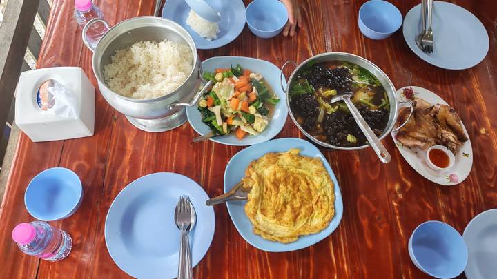 Simple Thai lunch spread with rice, omelette, soup and vegetables on a wooden table.