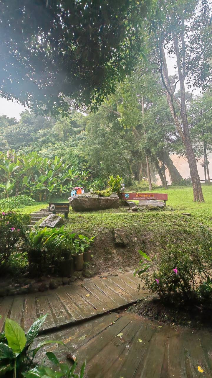Entrance signs and lush greenery at the base of a misty waterfall in a Thai national park.