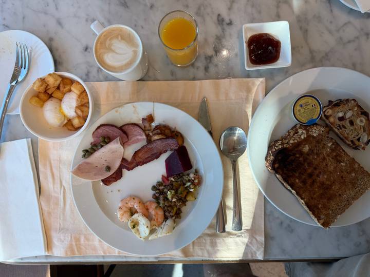 Breakfast table with toast, cold cuts, shrimp, salad, coffee and orange juice on marble surface.