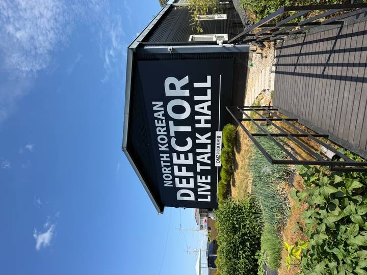 Black building with bold sign reading 'North Korean Defector Live Talk Hall' near the DMZ.