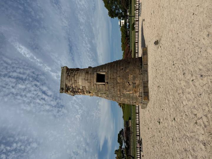Stone Cheomseongdae astronomical observatory stands against a textured sky in an open sandy field.