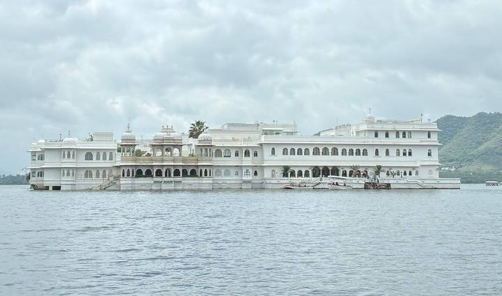 Elegant white Lake Palace floats on calm waters of Lake Pichola beneath cloudy skies.