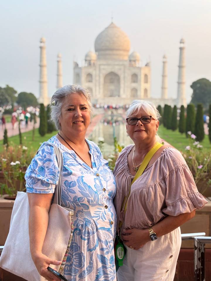 Two women smiling with the Taj Mahal softly out of focus behind them in warm evening light.