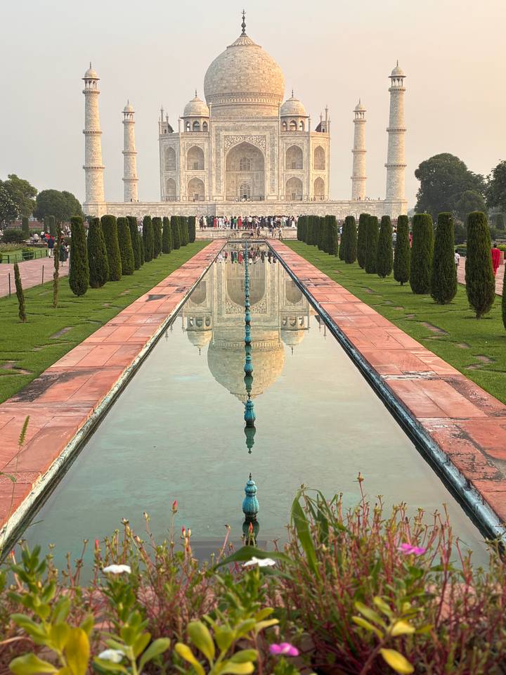 Symmetrical reflection of the Taj Mahal in the long pool flanked by cypress trees.
