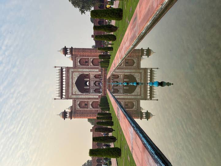 The grand main gateway to the Taj Mahal complex perfectly mirrored in the central pool.